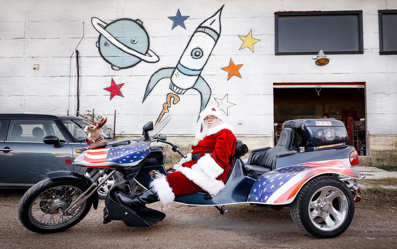 Santa reclines on a motorcycle in front of the Salado Glassworks