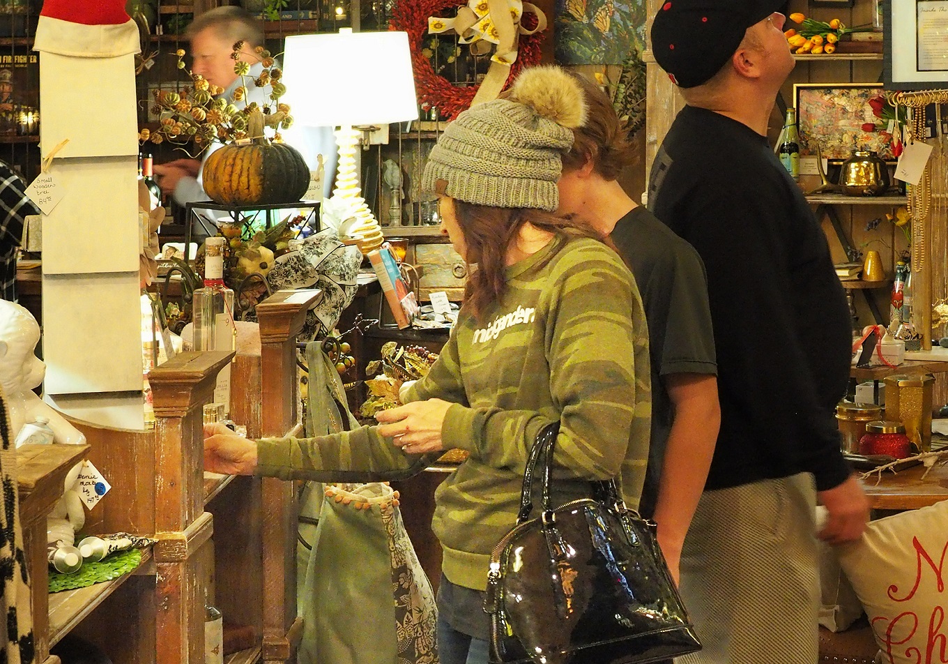 Woman wearing beanie examines items for sale in a shop decorated for Christmas